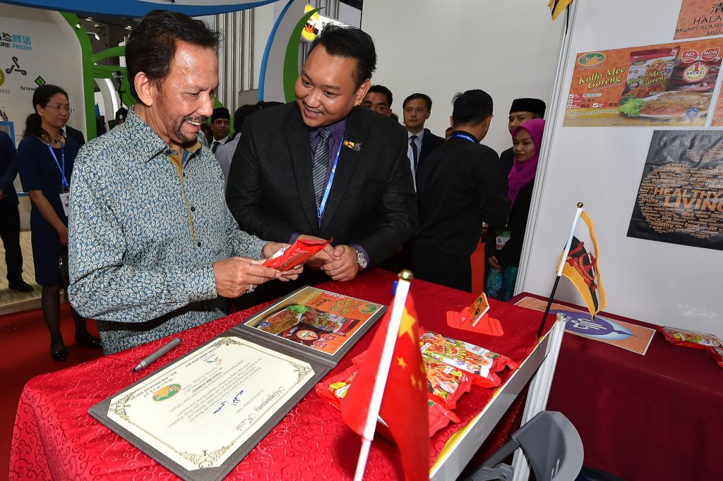 His Majesty looking at instant noodles made by Asli KTM, as their manager Haji Rani @ Haji Abdul Malek Haji Mohammad looks on.