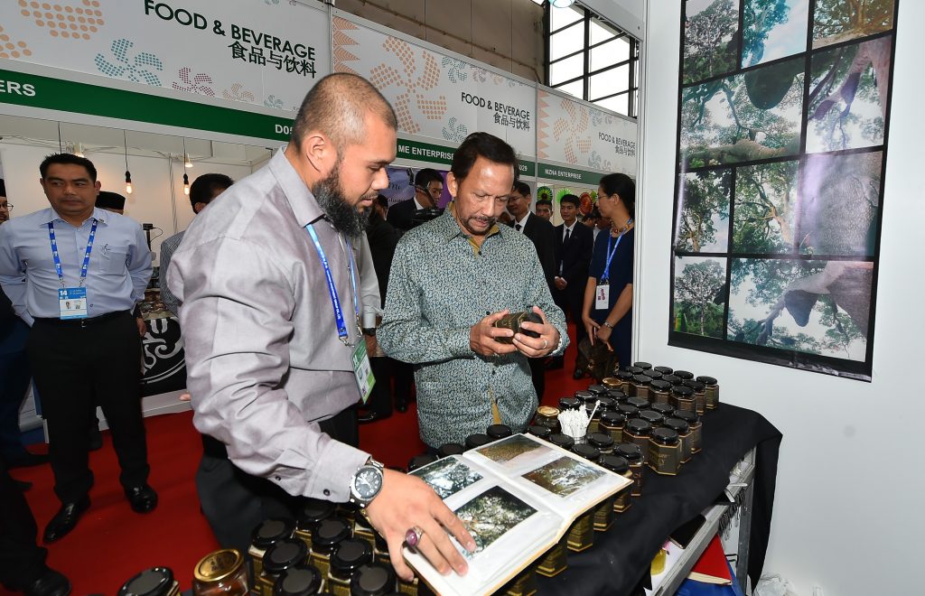 His Majesty looking at wild honey produced by Madu Maangaris, as its owner Firdaus looks on.